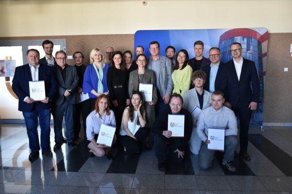 Grupowe zdjęcie uczestników konferencji studenckiej z dokumentami na tle ścianki UJW.