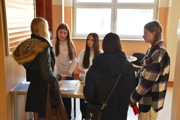 Uczestnicy rozmawiają z obsługą przy punkcie rejestracji wydarzenia.