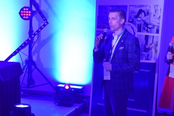 Mężczyzna w garniturze przemawia obok ekranu i planszy Rexroth.