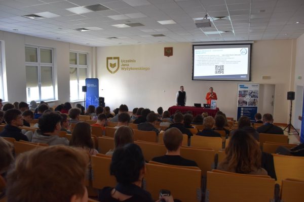 Publiczność w auli podczas prezentacji, na ekranie widoczny kod QR.