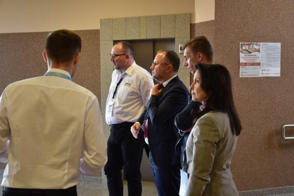 Uczestnicy konferencji rozmawiają w grupie w korytarzu uczelni.