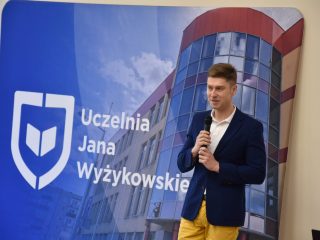 Prelegent z mikrofonem przed ścianką UJW podczas Dnia Drzwi Otwartych.
