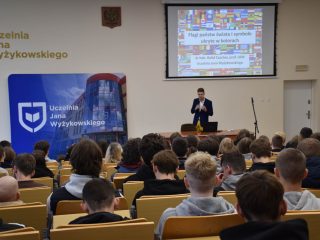 Prelegent przed publicznością w auli UJW; na ekranie prezentacja dotycząca życia i pracy w Chinach.
