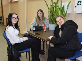 Trzy osoby siedzące przy niewielkim stoliku na korytarzu podczas Dnia Drzwi Otwartych.