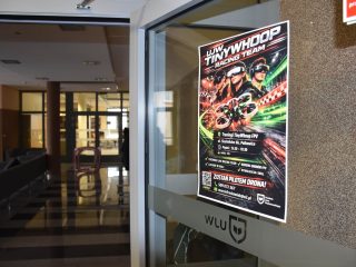 Plakat zespołu UJW Whoop Racing Team na szklanych drzwiach uczelni.