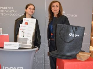 Dwie kobiety przy stoisku KGHM INOVA z ulotkami i torbą promocyjną.