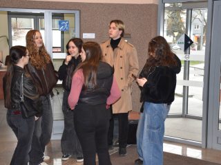 Grupa młodych osób rozmawia przy wejściu do budynku uczelni.