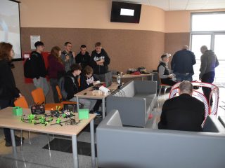 Sala pokazowa z małymi dronami, komputerami i torem przeszkód podczas Dnia Drzwi Otwartych.