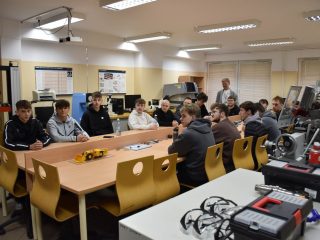 Uczestnicy siedzący przy stołach w pracowni technicznej z urządzeniami laboratoryjnymi.