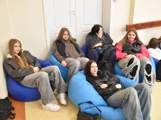 Uczestniczki spotkania siedzące na niebieskich pufach przy ścianie auli.