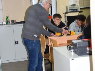 Prowadzący pochyla się nad stanowiskiem z urządzeniem w pracowni technicznej.