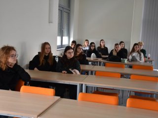 Grupa uczestniczek siedzi przy ławkach w jasnej sali zajęciowej.