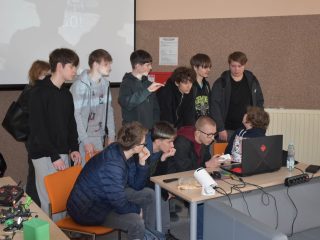 Uczestnicy skupieni przy laptopie na stanowisku pokazowym z dronami.