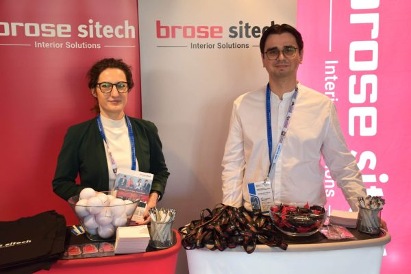 Dwoje przedstawicieli Brose Sitech przy stoisku z materiałami i gadżetami.