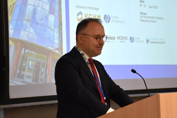 Mężczyzna w garniturze i czerwonym krawacie przemawia przy mównicy.