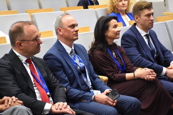Uczestnicy z identyfikatorami siedzą obok siebie w sali konferencyjnej.