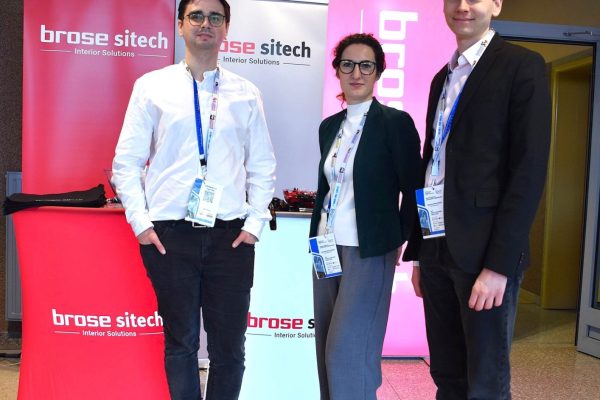 Troje uczestników konferencji pozuje przy stoisku Brose Sitech.