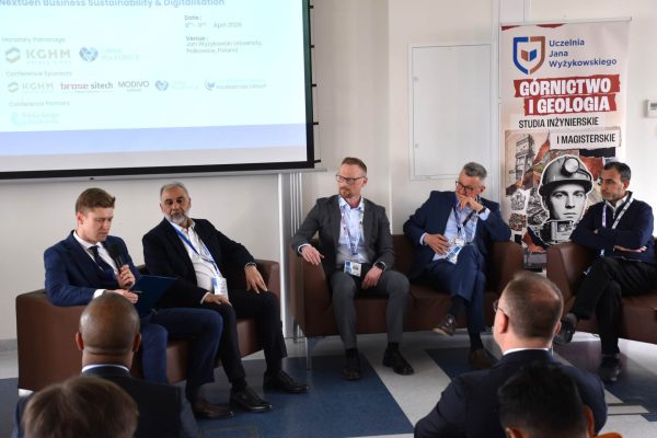 Moderator z mikrofonem otwiera dyskusję pięciu panelistów siedzących w fotelach.