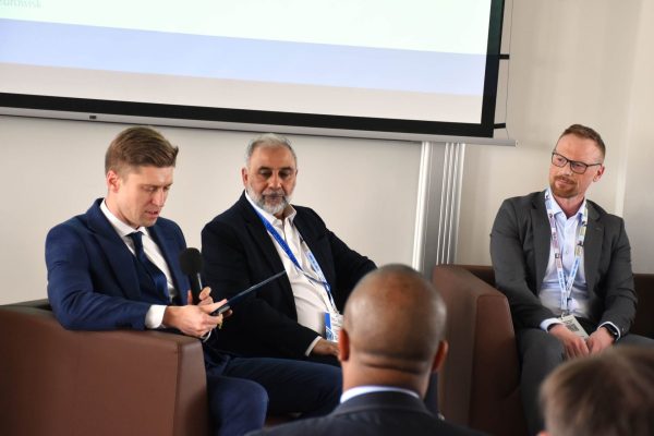 Moderator spogląda na notatki, obok siedzą dwaj paneliści.
