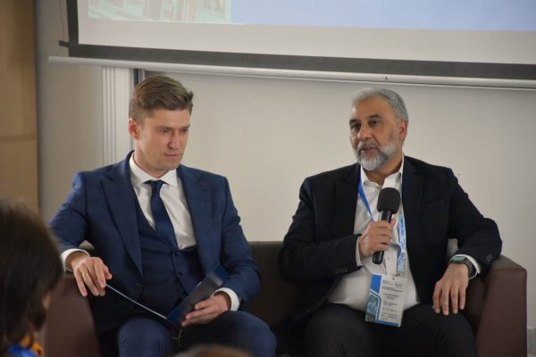 Brodaty panelista odpowiada do mikrofonu, moderator siedzi obok.