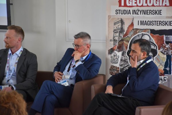 Trzej paneliści słuchają wypowiedzi, siedząc w brązowych fotelach.