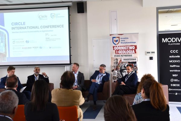 Panel dyskusyjny pod ekranem konferencji, z publicznością na pierwszym planie.