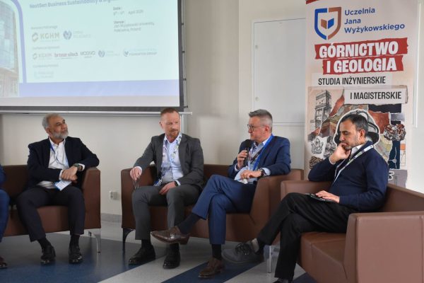 Czterej paneliści podczas dyskusji, mężczyzna w niebieskim garniturze mówi do mikrofonu.