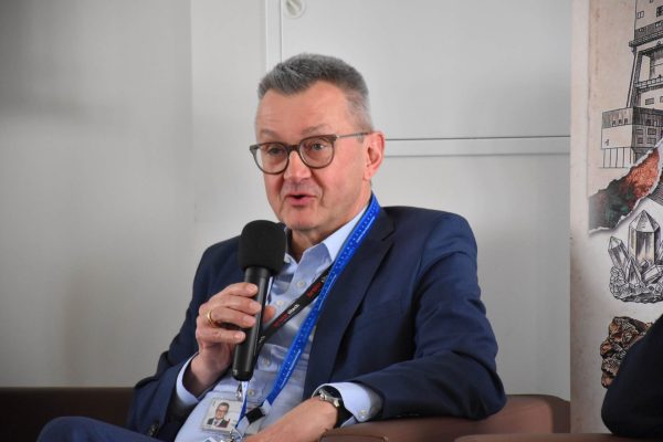 Zbliżenie na panelistę w okularach przemawiającego do mikrofonu.