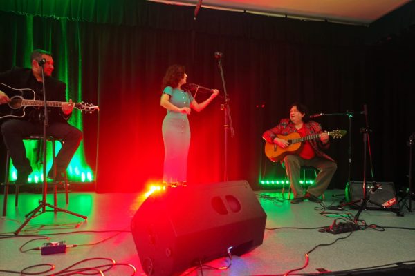 Skrzypaczka i dwaj gitarzyści występują na scenie oświetlonej na czerwono i zielono.