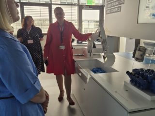 Prowadząca w czerwonej sukience omawia stanowisko demonstracyjne Bosch Rexroth.