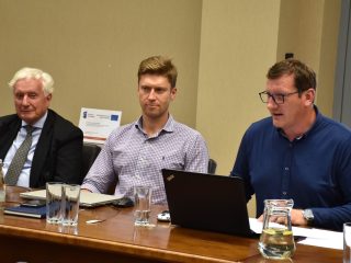 Trzej uczestnicy posiedzenia Senatu UJW siedzą przy stole; jeden korzysta z laptopa.