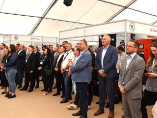 Uczestnicy wystawy Mercuriusz stoją w hali namiotowej i słuchają wystąpienia.