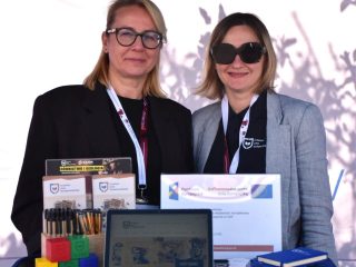 Dwie przedstawicielki UJW stoją za ladą z laptopem i materiałami promocyjnymi.