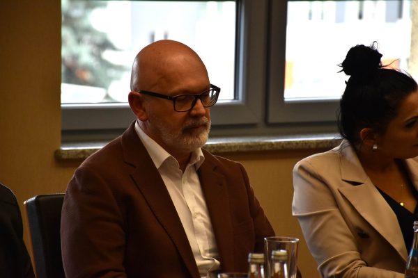 Uczestnik w brązowej marynarce i okularach słucha obrad.