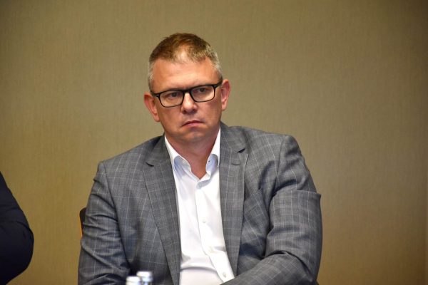 Uczestnik w okularach i szarej marynarce w kratę podczas posiedzenia.