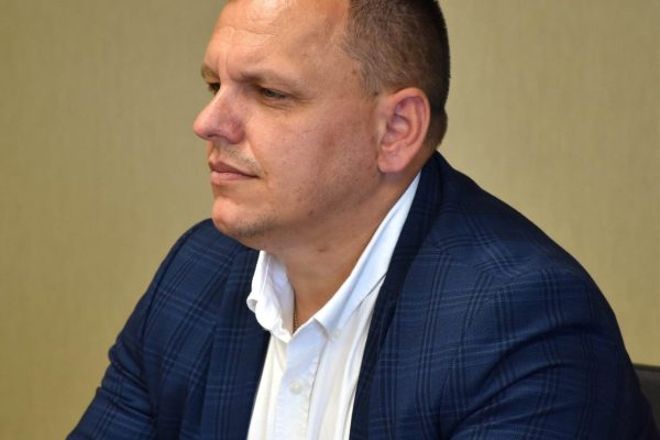 Uczestnik w granatowej marynarce słucha dyskusji przy stole.