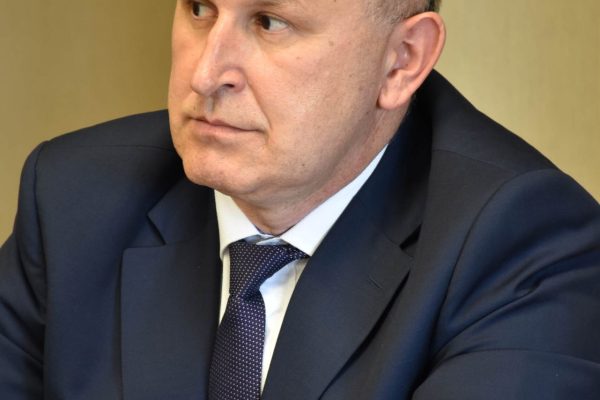 Uczestnik w garniturze z okularami na głowie słucha obrad.