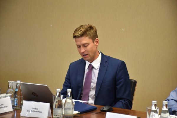 Uczestnik w granatowym garniturze odczytuje dokument przy laptopie.