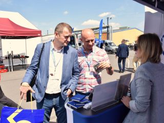 Dwaj mężczyźni rozmawiają z przedstawicielką UJW przy ladzie z materiałami promocyjnymi.