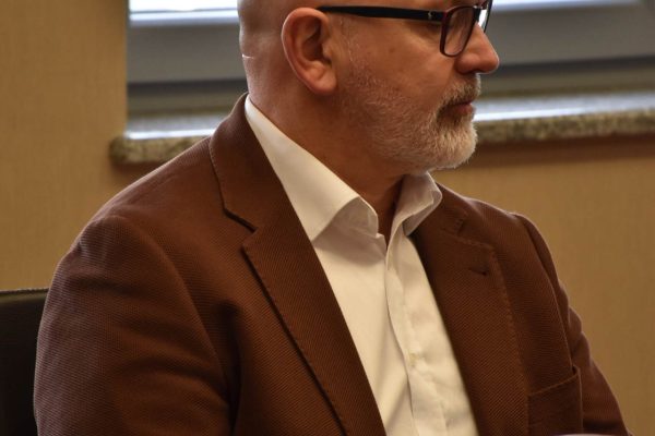 Mężczyzna w brązowej marynarce siedzi przy stole z naczyniami.