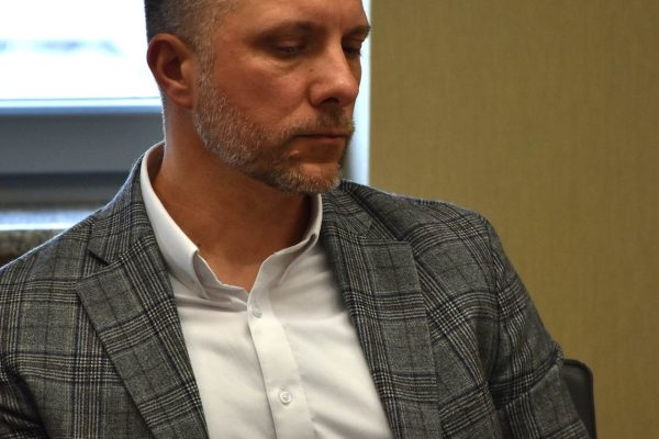 Uczestnik w szarej marynarce w kratę przy stole konferencyjnym.