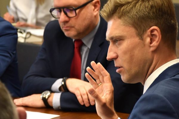 Uczestnik w granatowym garniturze gestykuluje podczas posiedzenia.
