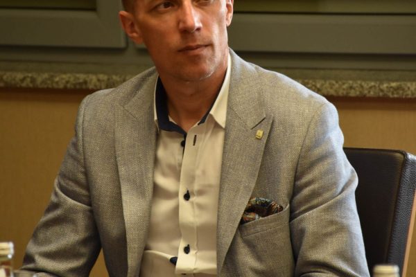 Mężczyzna w jasnoszarej marynarce siedzi przy dokumentach.
