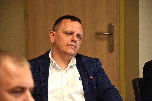 Uczestnik w granatowej marynarce słucha posiedzenia.