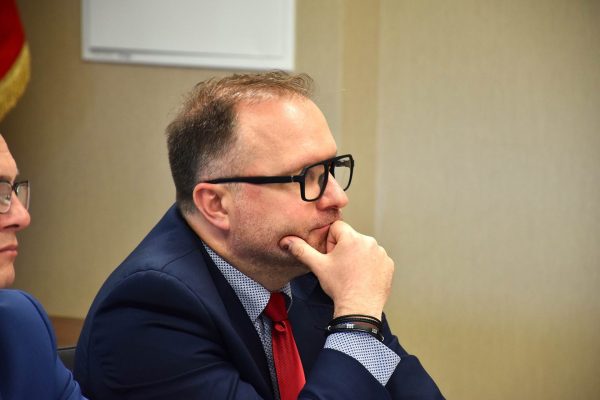 Mężczyzna w okularach i czerwonym krawacie słucha dyskusji.