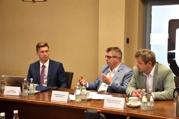 Mężczyzna w jasnoniebieskiej marynarce gestykuluje podczas dyskusji.