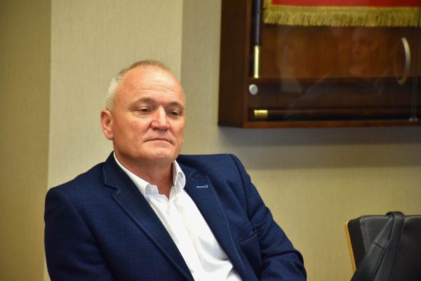 Uczestnik w granatowej marynarce siedzi pod sztandarem.