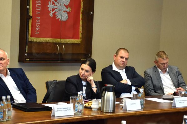 Członkowie Konwentu siedzą przy stole pod sztandarem z godłem Polski.