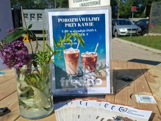 Stolik z ulotkami UJW i planszą „Porozmawiajmy przy kawie”.
