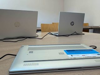 Laptopy na stole, jeden odwrócony spodem z etykietą dofinansowania.